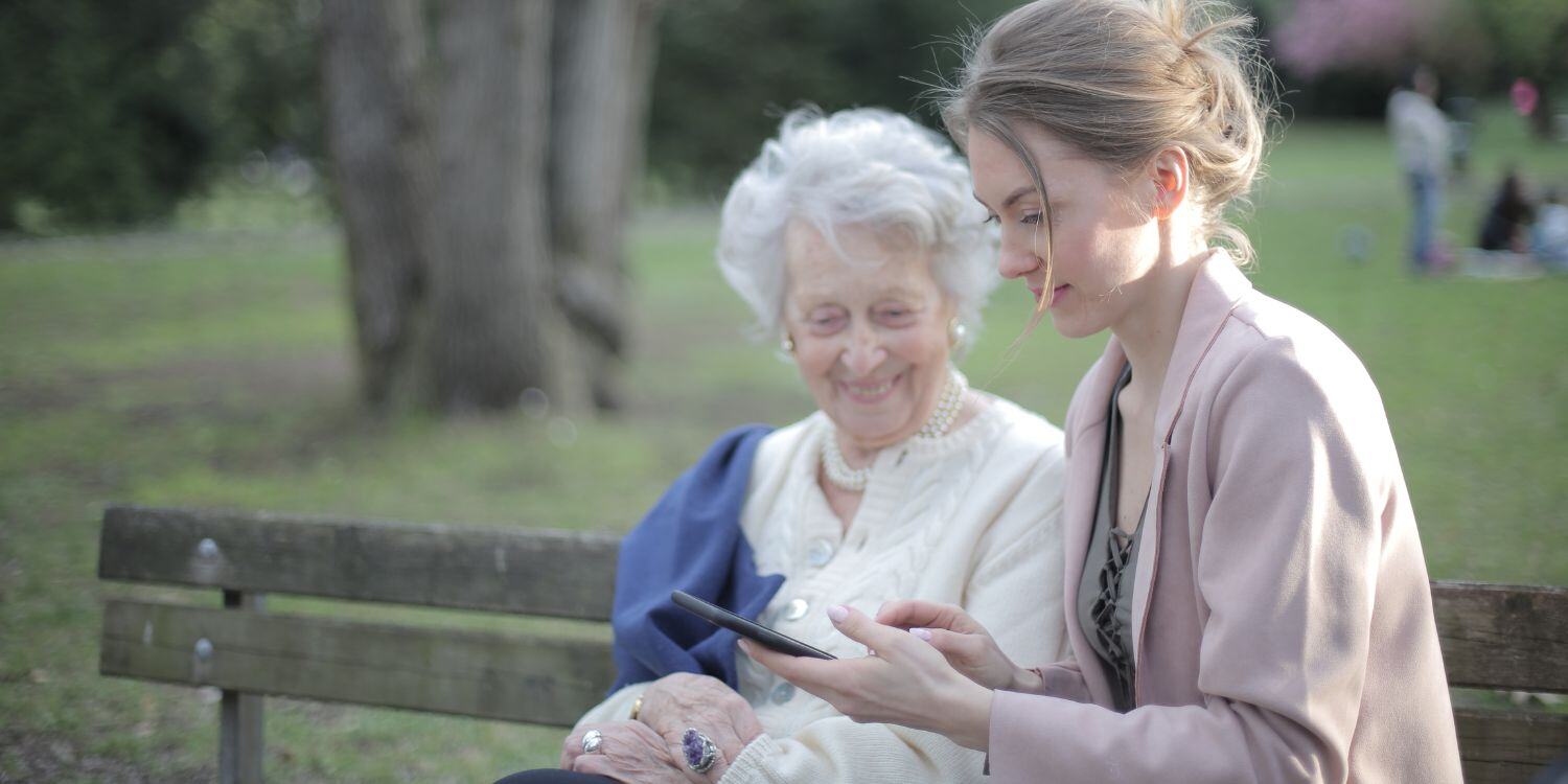 Woman texting on smartphone as senior woman looks over her shoulder.