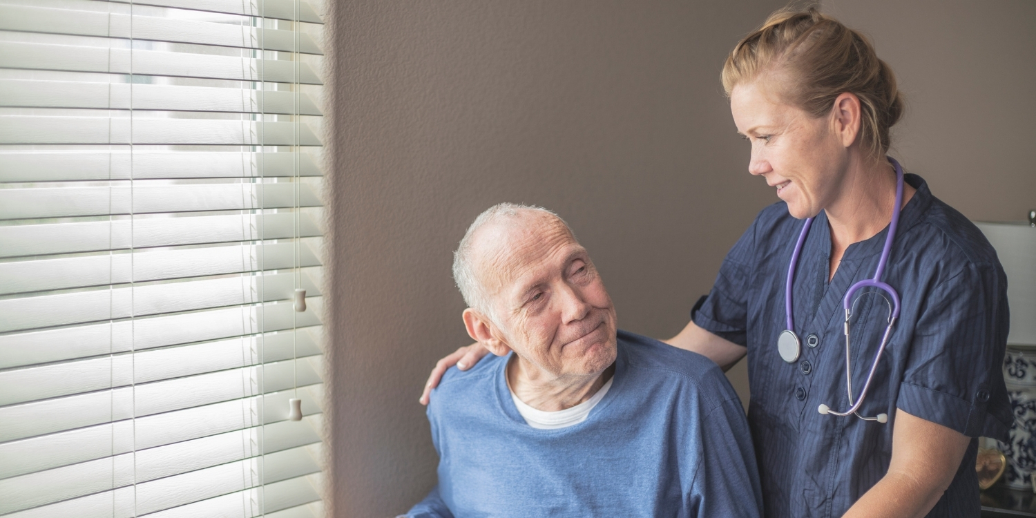 Caregiver standing beside elderly patient.