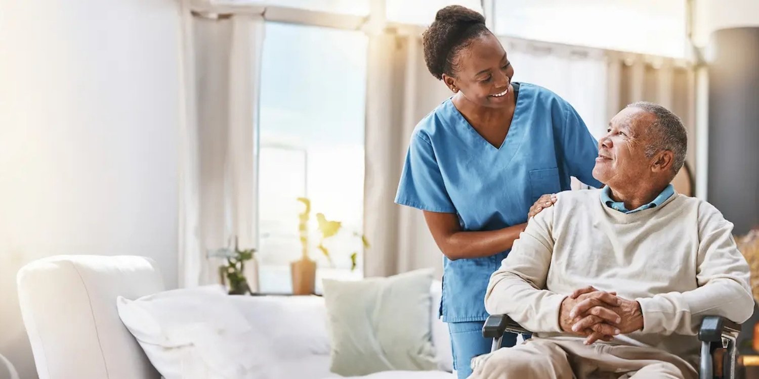 Hospice caregiver standing beside elderly patient in wheelchair.