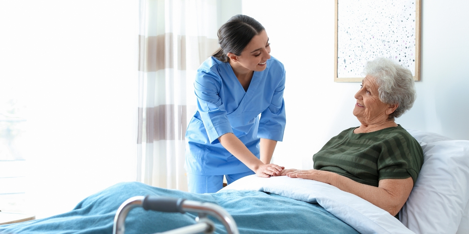 Smiling clinician holding a patient's hand at bedside.