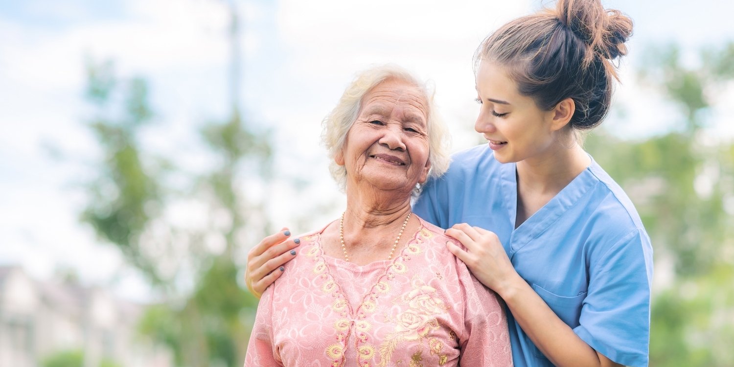 Smiling elderly patient standing with caregiver outdoors.