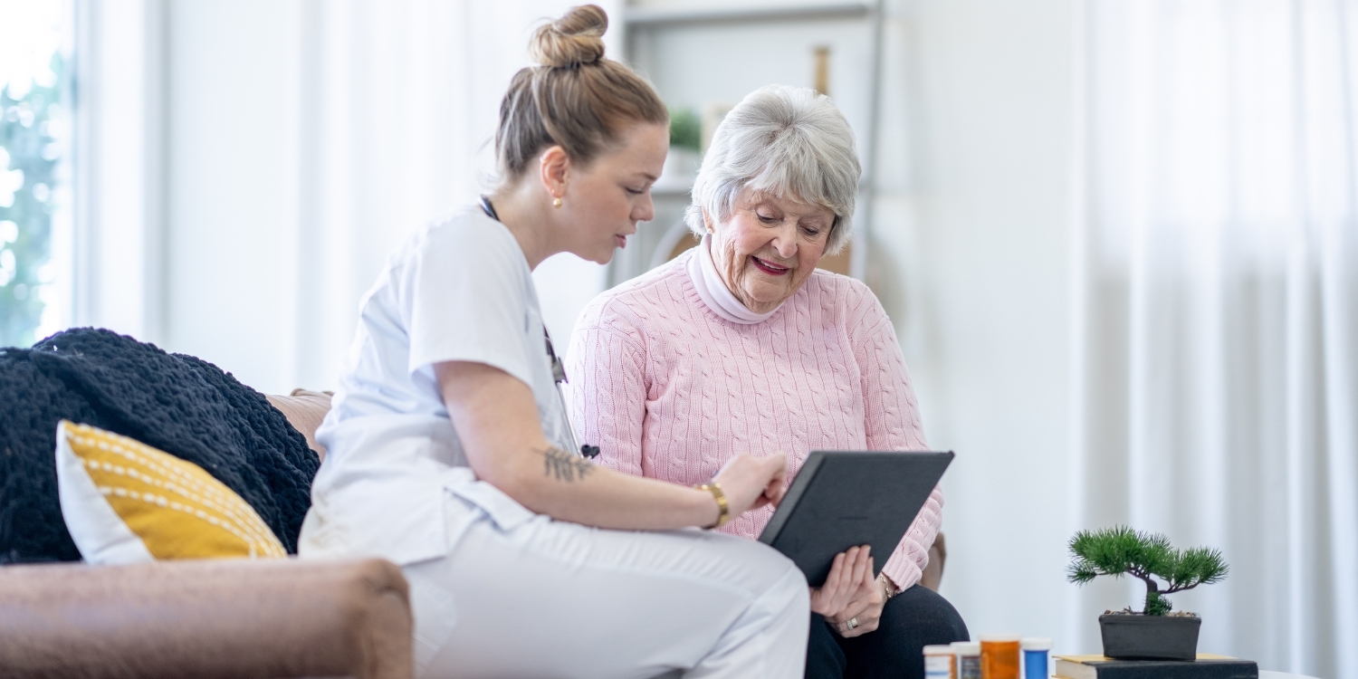 Caregiver viewing a tablet device with an elderly patient.