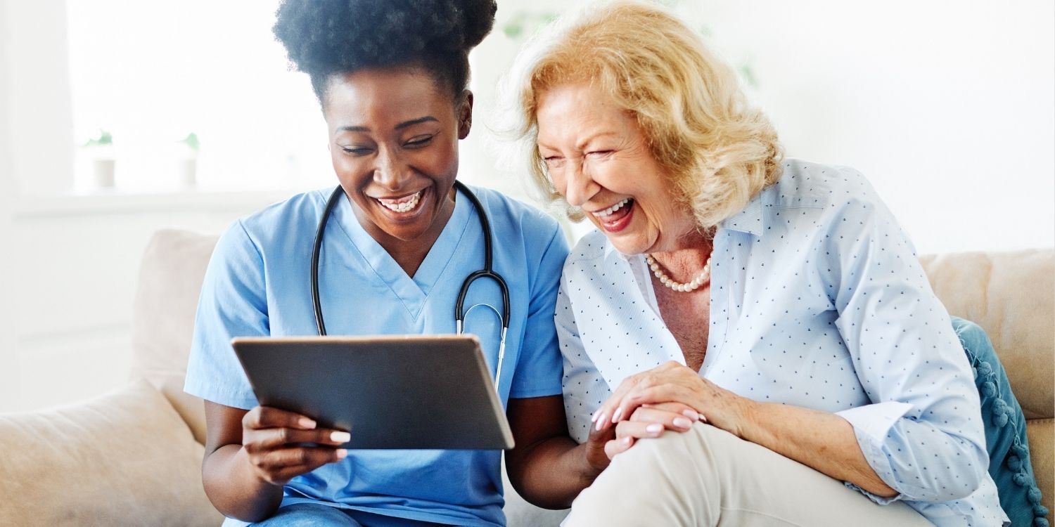 Smiling nurse showing an older woman information on a tablet as they both are enjoying the interaction